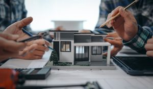 Hands discussing a 3D architectural model of a house, illustrating collaboration in drafting and design technology education at ITI Technical College.