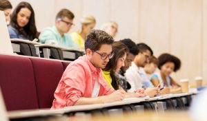 education, technical School, learning and people concept - group of international students with notebooks writing in lecture hall