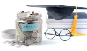 education budget concept. education money savings in a glass jar with glasses, graduate hat and book isolated on white background