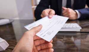 Close-up Of A Businessperson's Hand Giving Cheque To Colleague At Workplace