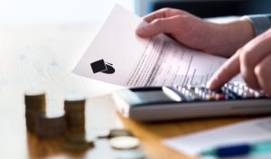 Man counting college savings fund, tuition fee or student loan with calculator. Education price and expenses concept. Money and papers on table. Calculating budget and planning finance.
