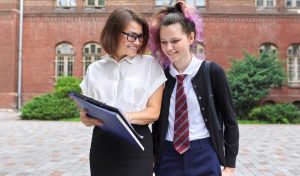 Outdoor portrait of talking female teacher and student teenager. Campus, school building background, back to college, back to school, start of classes