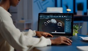 Tired african designer engineer analyzing new prototype of 3D model of industry product, working overtime. Industrial female worker studying gears idea on laptop showing cad software on device display