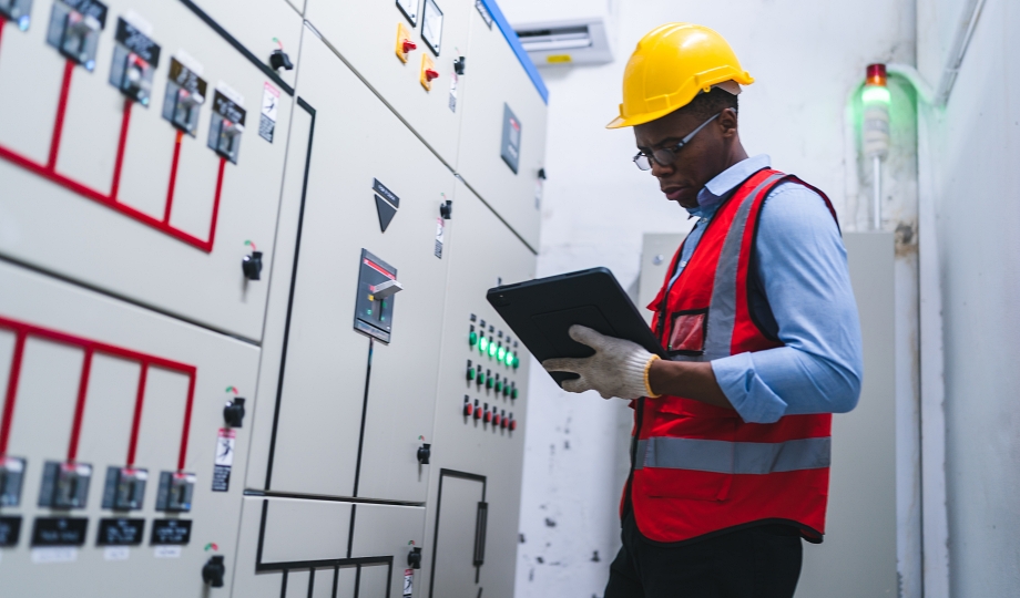 Technician of modern factory checking to automatic machinery. Black worker with clipboard programmable logic controller to manage large machine working full industrial automatic