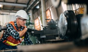 worker is working on a lathe machine in a factory. Turner worker manages the metalworking process of mechanical cutting on a lathe