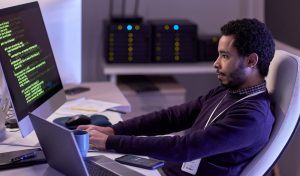 Side view portrait of bearded man using computers and writing code in neon light