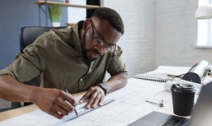 Afro-American architect working in office with blueprints.Engineer inspect architectural plan, sketching a construction project. Portrait of black handsome man sitting at workplace. Business concept.