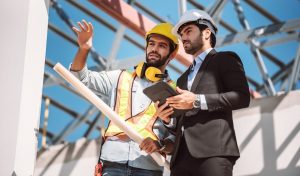 Civil engineer and construction worker manager holding digital tablet and blueprints , talking and planing about construction site.  Cooperation teamwork concept.