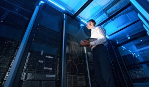 Server administrator of data center with laptop in one hand checking network cabinet