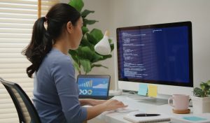 Asia young business woman sit busy at home office desk work code on desktop PC reskill upskill for job career remote self test IT deep tech ai design skill online html text for cyber security.