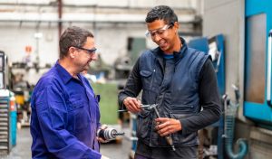 Instructor teaching and speaking the trade to a metal industrial factory worker in the numerical control sector