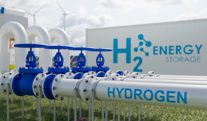 Blue and white hydrogen pipeline valves with H2 Energy Storage signage and wind turbines in the background
