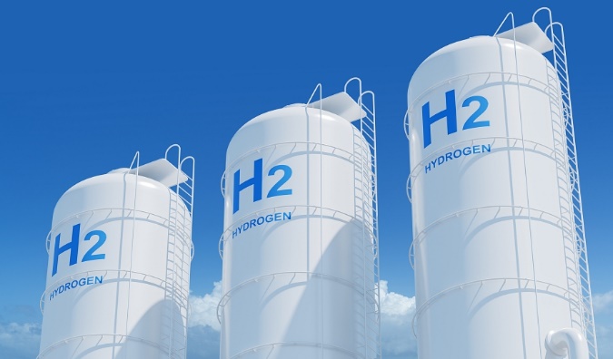 Three large white H2 hydrogen storage tanks standing against a clear blue sky