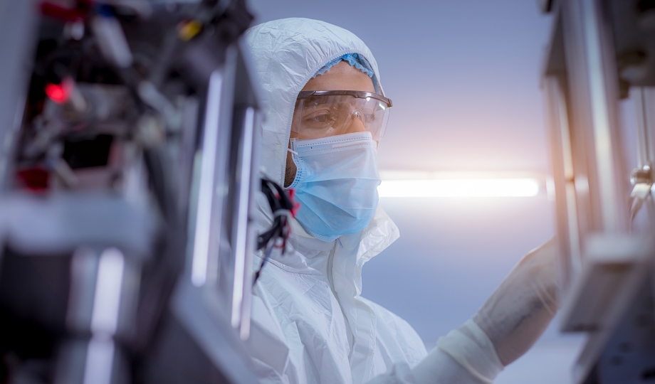 Process technician in cleanroom PPE inspecting pharmaceutical manufacturing equipment