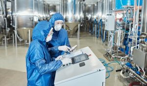 Two process technicians in protective suits operating equipment on a pharmaceutical production floor