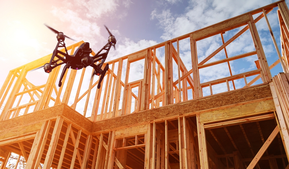 Drone flying above a wood-framed construction site under a blue sky