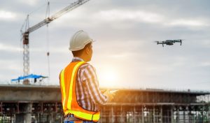 Construction worker in a hard hat and safety vest piloting a drone at a job site