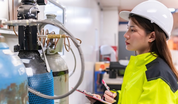 Process technology technician in a hard hat and safety jacket inspecting hydrogen gas cylinders in an industrial facility