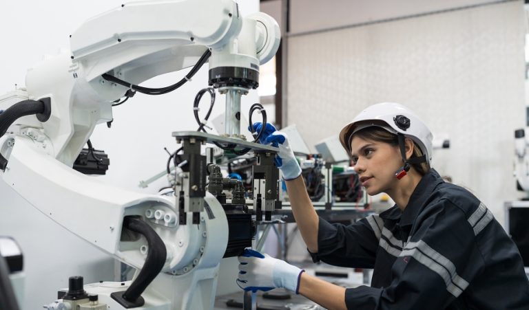 Technician in a white hard hat and gloves inspecting an industrial robot arm