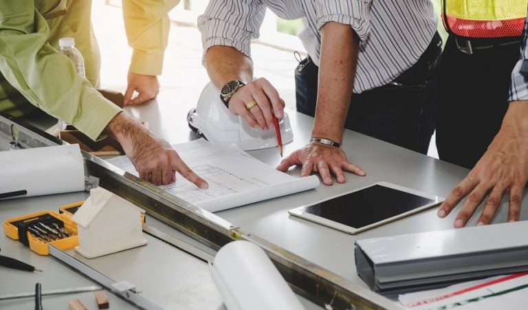 Construction estimator reviewing building plans and a tablet at a work table