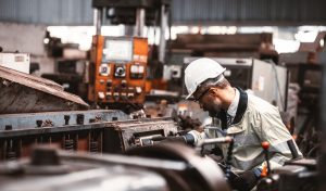 Technician in a white hard hat and safety jacket working on industrial machinery during equipment disconnection